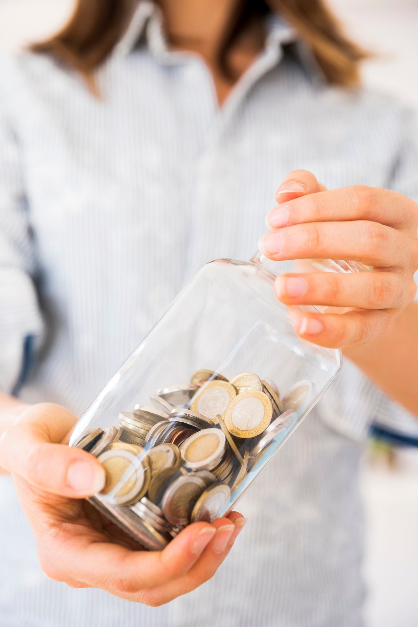 Una mujer sostiene un frasco lleno de monedas de euro.