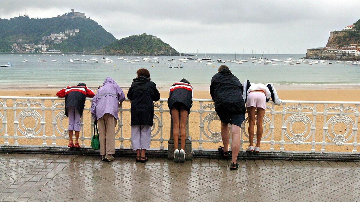 Una familia de turistas se asoma a la playa de la Concha de Donostia totalmente vacía tras las fuertes lluvias registradas.