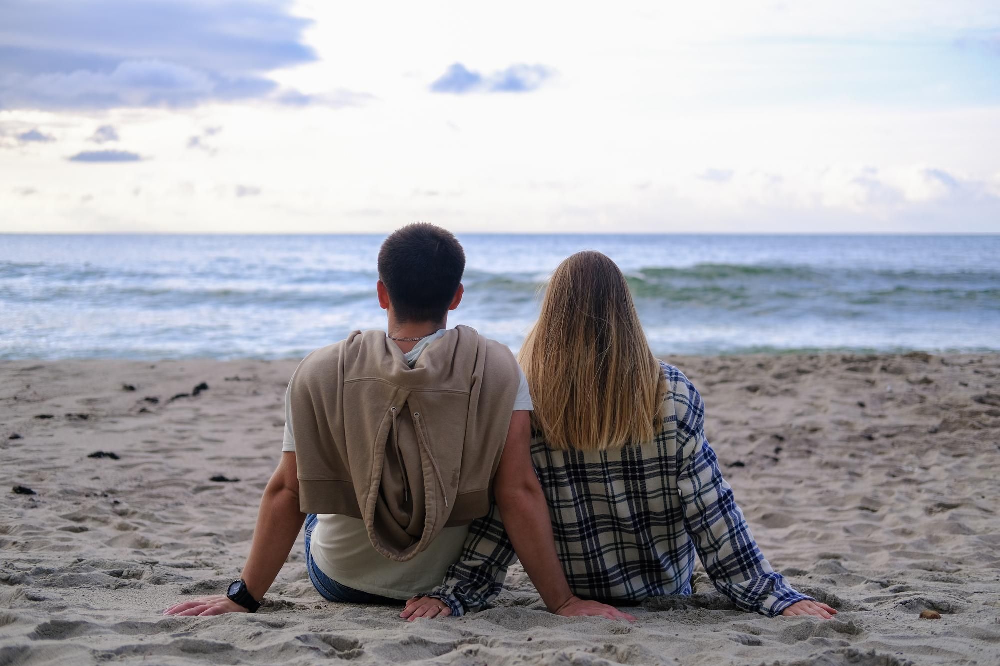 Dos adolescentes sentados en la arena mirando al mar.