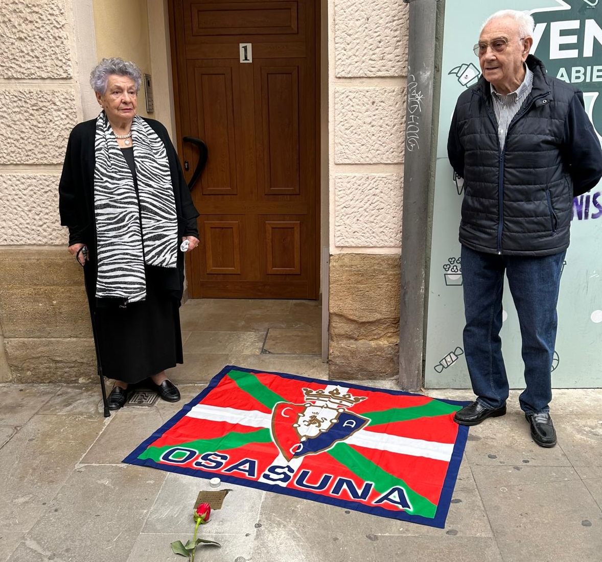 Mikele Aguirre, hija de Fortunato, junto con Antontxu y la bandera de Osasuna desplegada cerca de la placa de homenaje.
