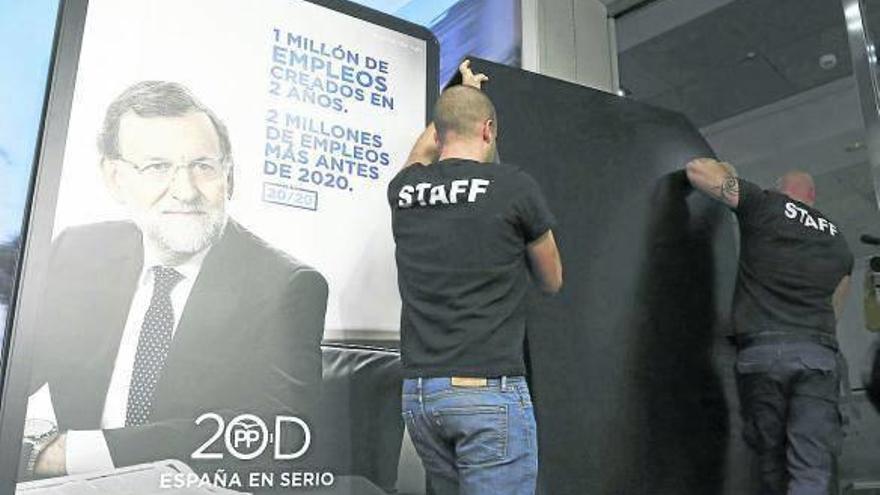 Dos operarios descubren uno de los carteles del PP para las elecciones generales.