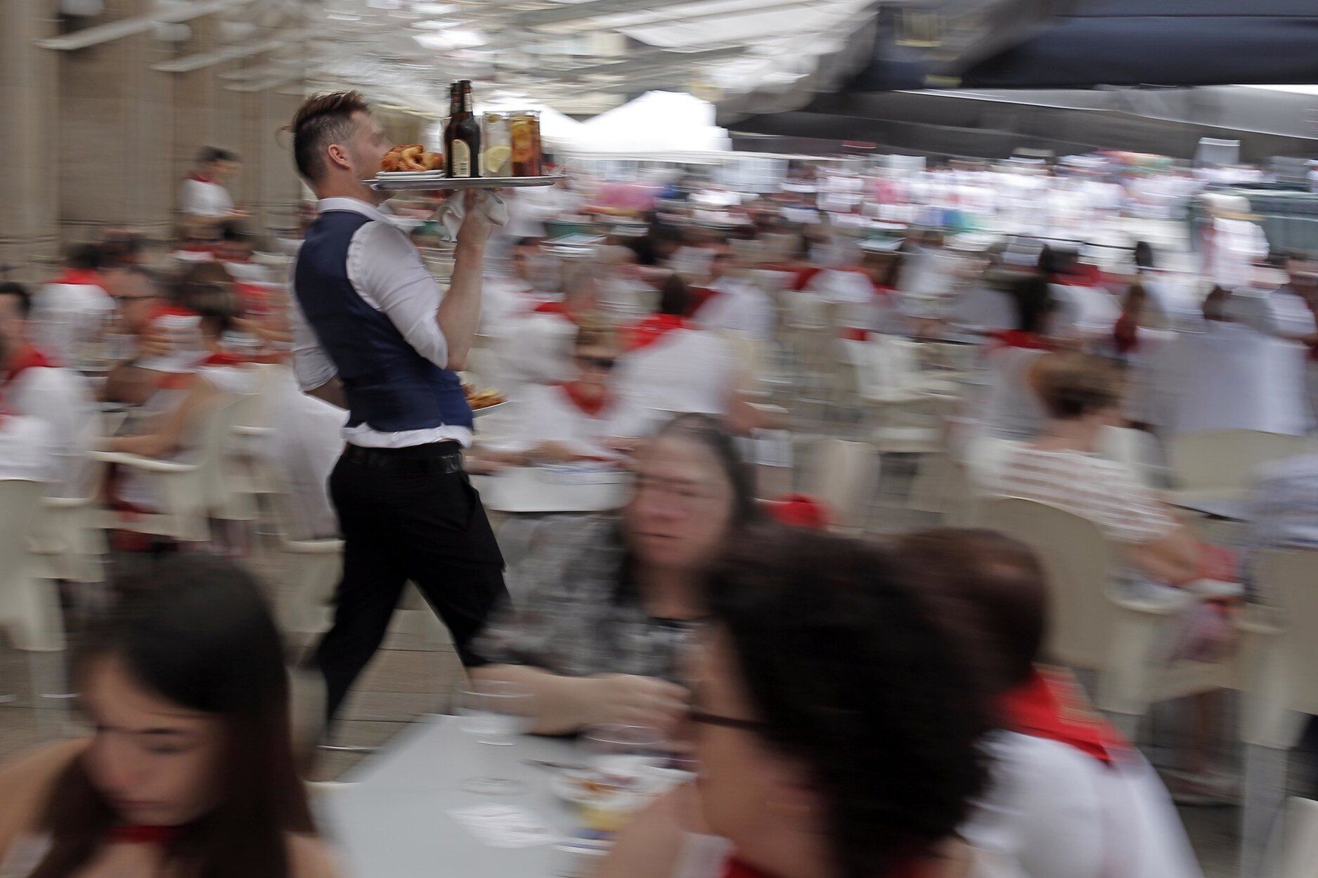 Un camerero lleva una bandeja entre la gente en las terrazas de San Fermín de la Plaza del Castillo.