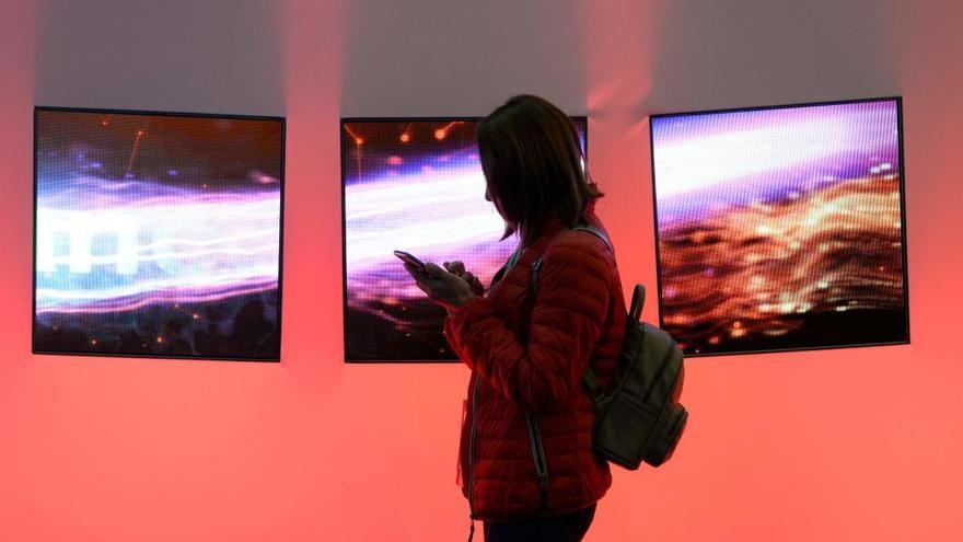 Una mujer consulta el móvil frente a pantallas de televisión