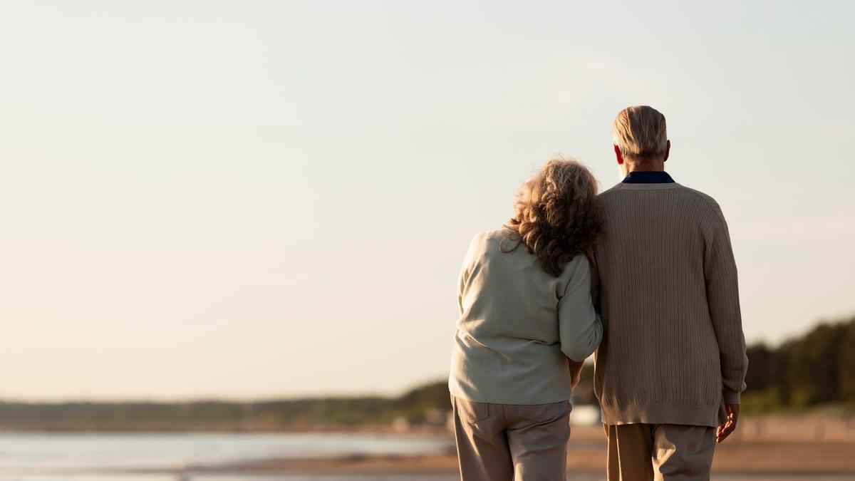 Una pareja de pensionistas  pasea por la playa.