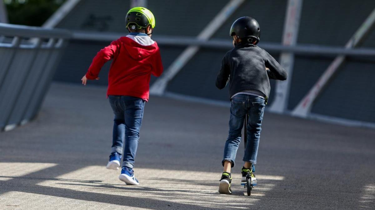 Dos niños jugando, uno de ellos montado en un patinete.