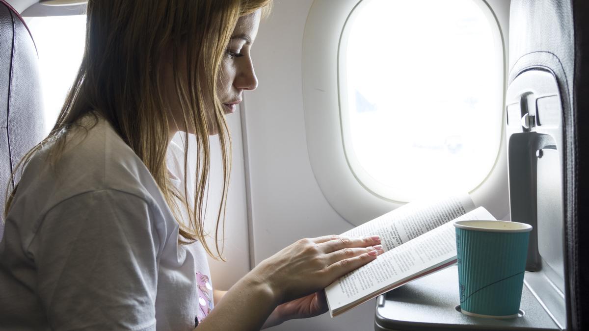 Mujer lee un libro en el avión mientras bebe agua