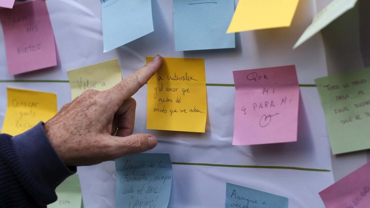 Un señor pega un post-it en el panel instalado en el stand informativo.
