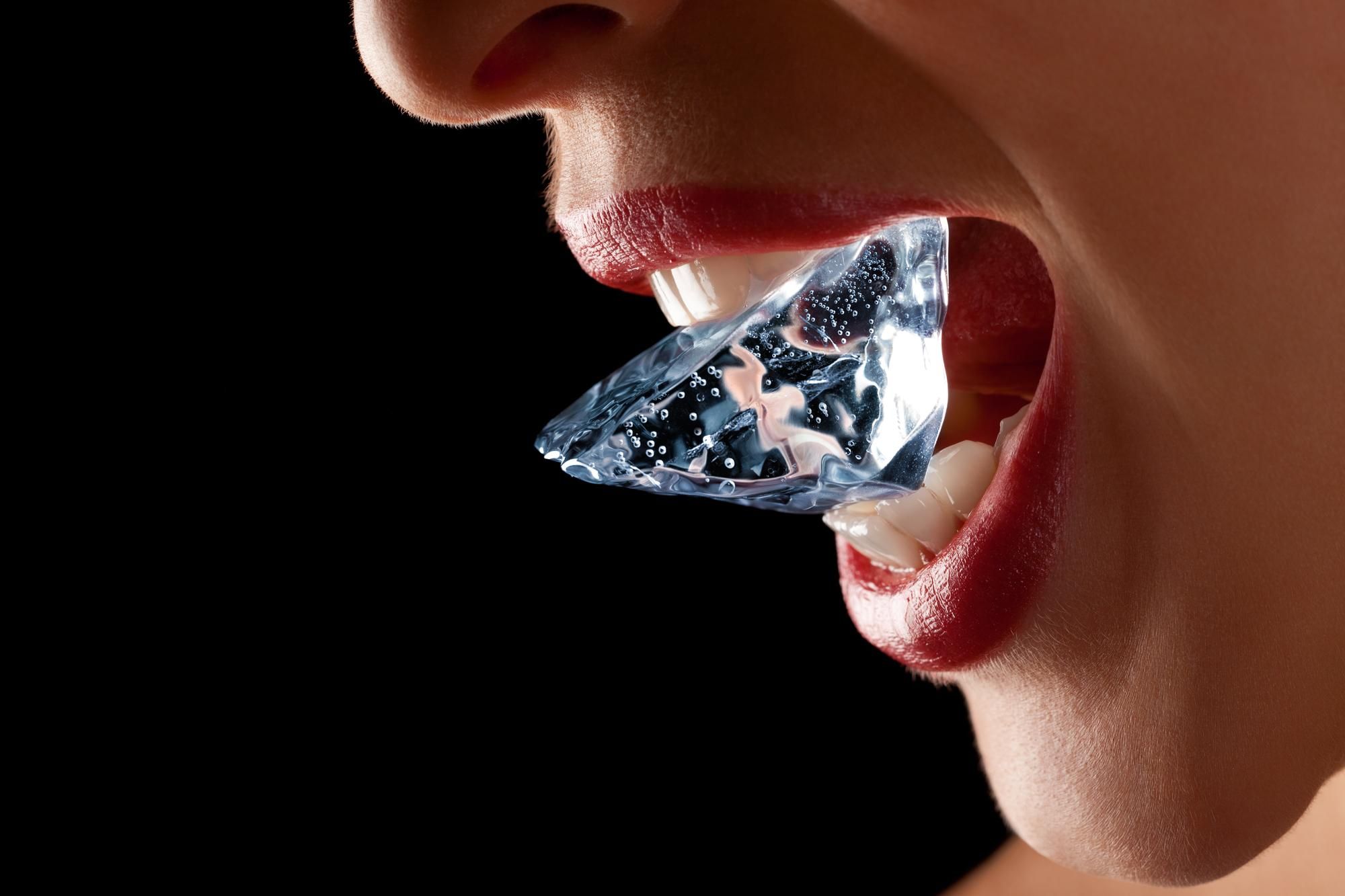 Una mujer sujeta un cubito de hielo con los dientes.