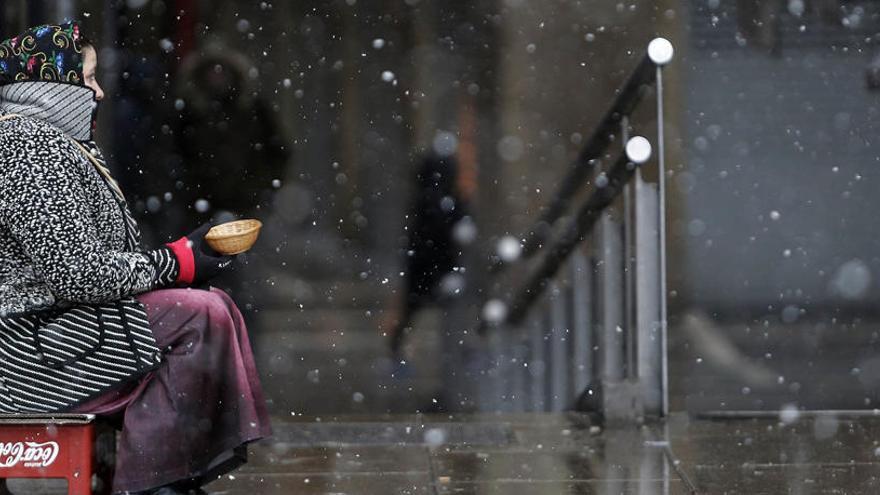 Una mujer pide limosna en el Casco Antiguo de la capital Navarra bajo la nieve.