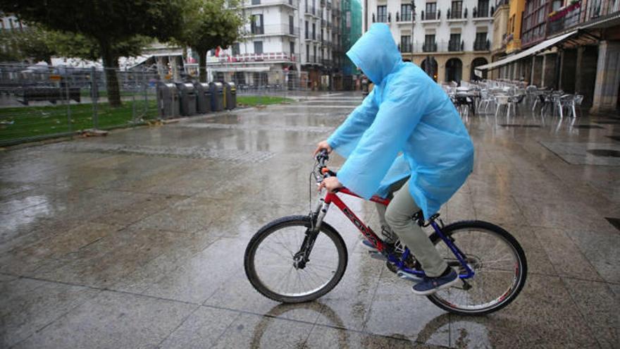 Un ciclista, resguardado de la lluvia con un chubasquero, a su paso por la Plaza del Castillo.