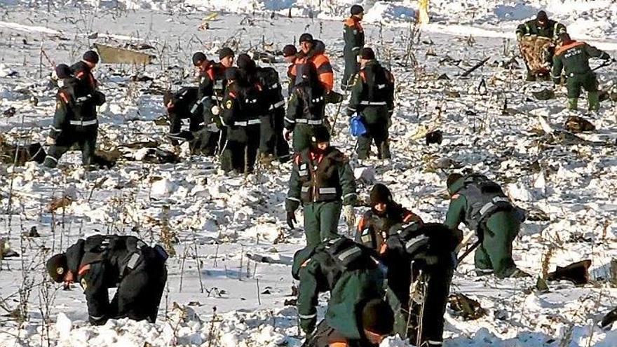 Miembros de los equipos de rescate buscan bajo la nieve en el lugar en el que se estrelló el avión.