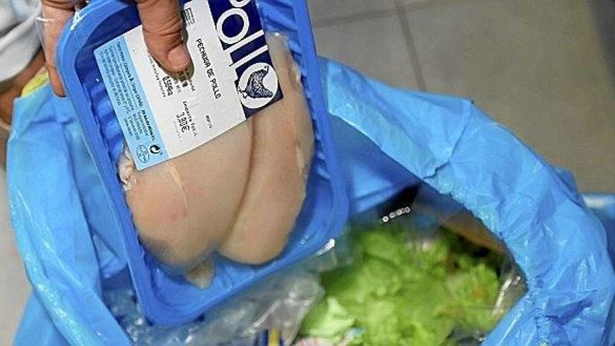 Una persona echa a la bolsa de la basura llena de comida una bandeja de pollo caducado.