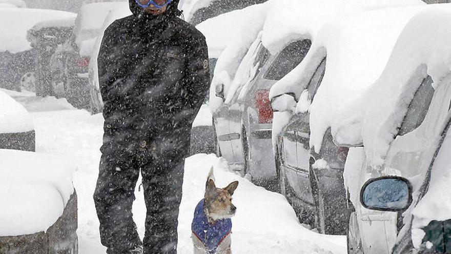 Un vecino camina junto a su perro por unas calles cubiertas de nieve.