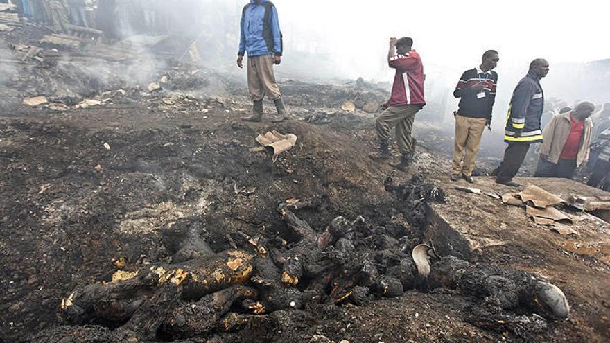 Personas caminan cerca de cuerpos carbonizados en el barrio de Lunga Lunga, cerca de Nairobi, Kenia.