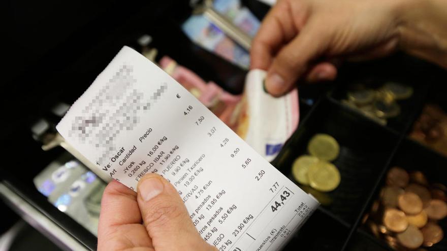 Un comerciante observa un tique de una compra efectuada en su local antes de entregárselo a su cliente.