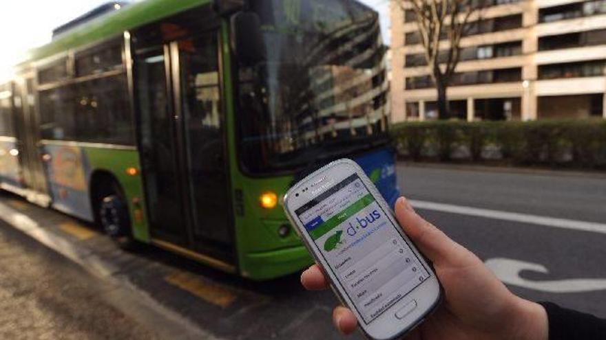Una persona comprueba el tiempo de espera de los autobuses en un móvil, frente a un vehículo de Dbus.