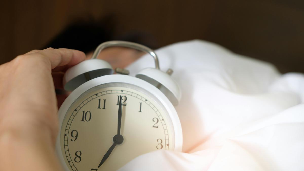 Una persona con un reloj despertador en la cama.