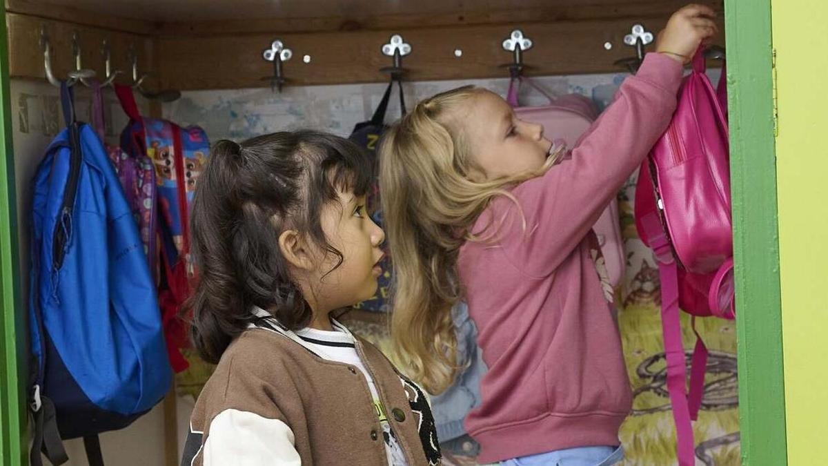 Dos niñas cuelgan sus mochilas en un perchero.