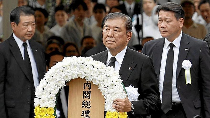 El primer ministro japonés, Shigeru Ishiba, sostiene una corona de flores. A la derecha, varias personas rezan durante una homilía por las víctimas de la bomba atómica.  | EFE