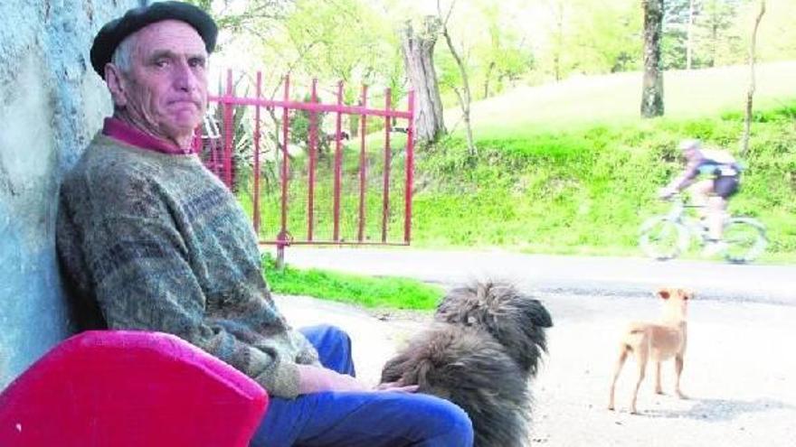 Andrés Zufiria mira a la cámara, mientras sus perros observan a un ciclista que pasa por delante del caserío Atagoiti.