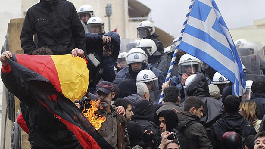Un manifestante quema una bandera de Alemania (i) mientras otros tratan de irrumpir en el Parlamento griego en Atenas.