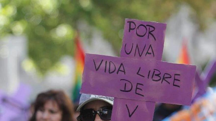 Una mujer muestra una cruz con una frase contra la violencia machista.