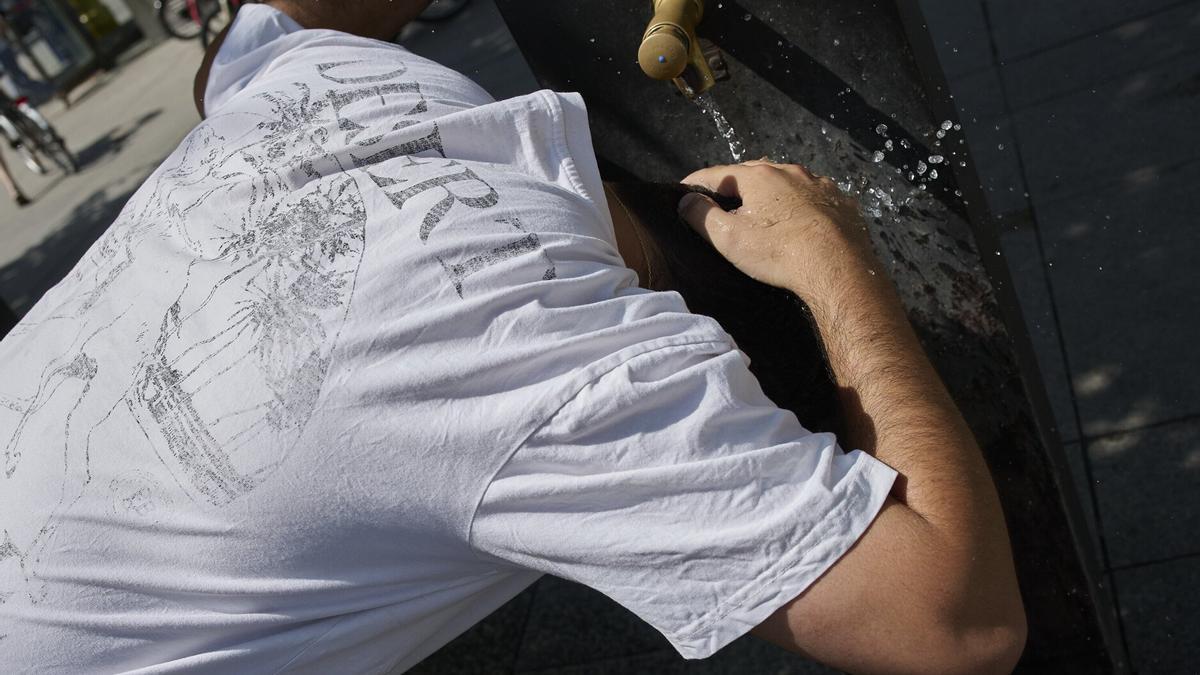 Un joven se refresca en una fuente.
