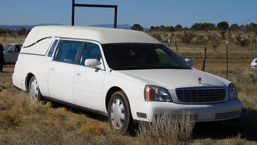 Un coche fúnerbe a la entrada de un cementerio.