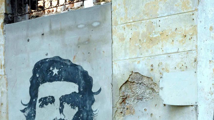 Una mujer permanece apoyada en un árbol junto a un retrato del Che Guevara con el lema &quot;Hasta la victoria siempre&quot;.