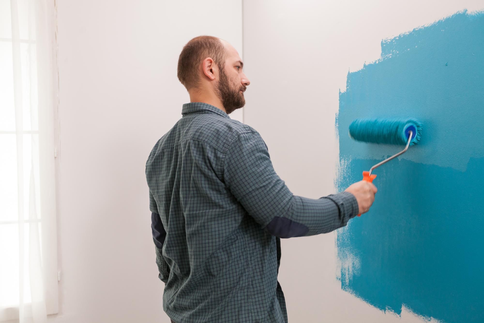 Un hombre pinta la pared de una vivienda con pintura azul.