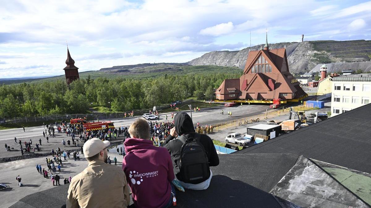 Tres jóvenes observan desde la distancia el traslado de la iglesia de Kiruna, en Suecia.