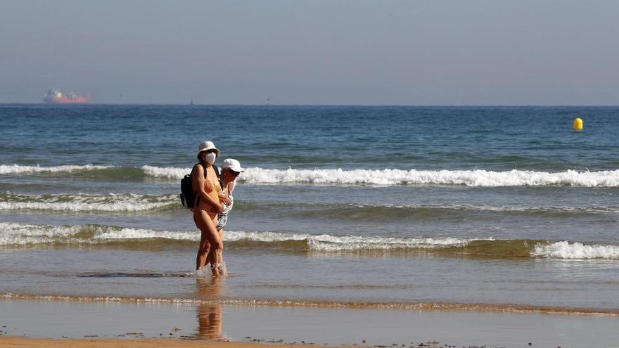 Dos personas pasean por la playa con mascarilla