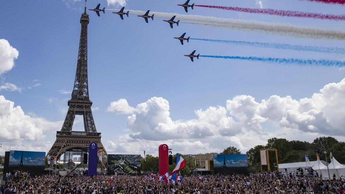 Una multitud ondea banderas francesas frente a la Torre Eiffel durante la transmisión de la ceremonia de traspaso olímpico entre los Juegos Olímpicos de Tokio y los de París.