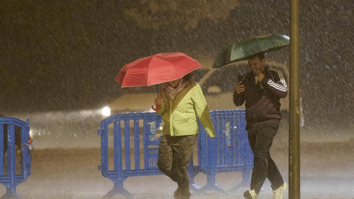 Dos personas se protegen de la lluvia con paraguas durante una fuerte tormenta.