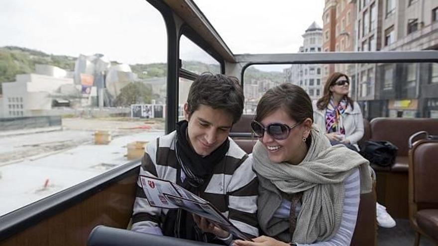 Un grupo de turistas lee un folleto a bordo del autobús turístico de Bilbao.