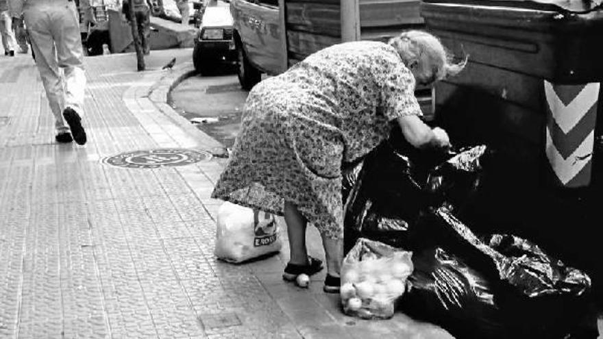 Una señora rebusca entre varias bolsas de alimentos tiradas junto a los contenedores de basura.