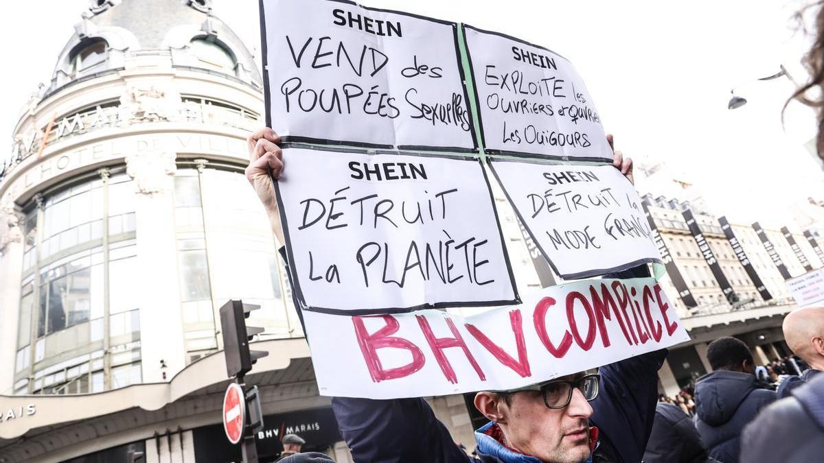 Un hombre levanta un cartel de protesta contra Shein en la inauguración de su primera tienda física en parís.
