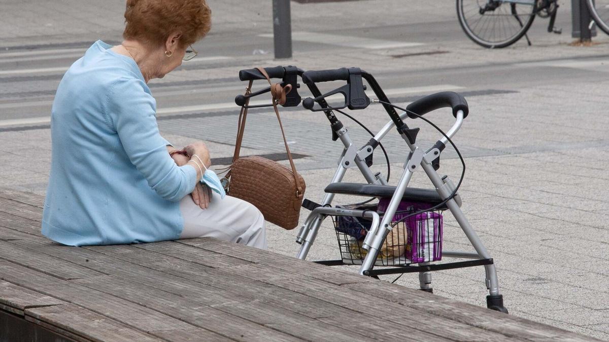 Una mujer mayor descansa en un banco de la calle.