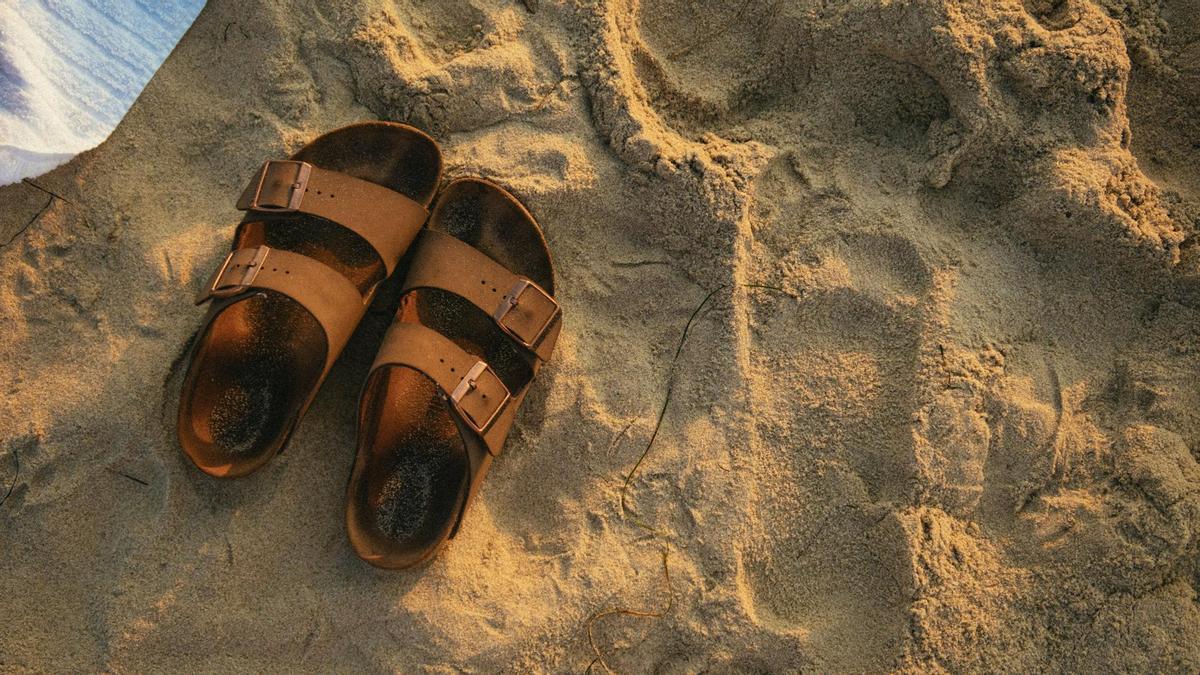 Sandalias sobre la arena con la huella del pie marcada.