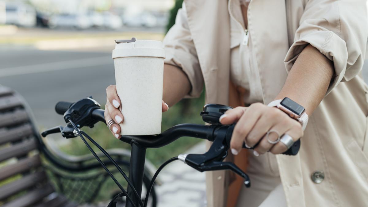 Una mujer toma un café mientras anda en bici.
