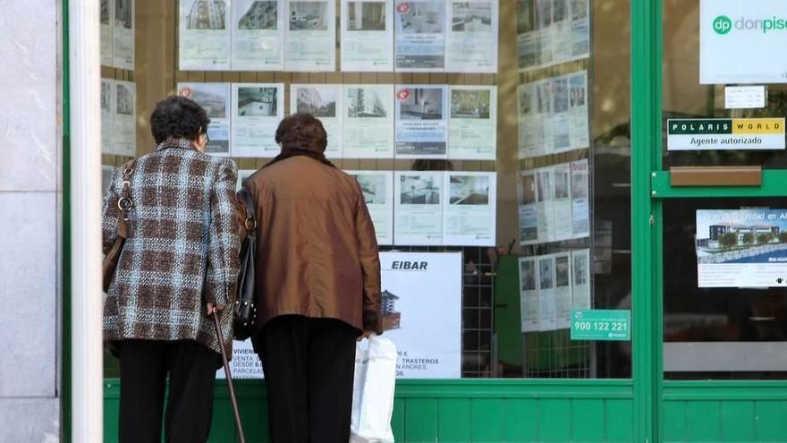 Dos mujeres comparan las diferentes ofertas de pisos en venta ante el escaparate de una inmobiliaria.