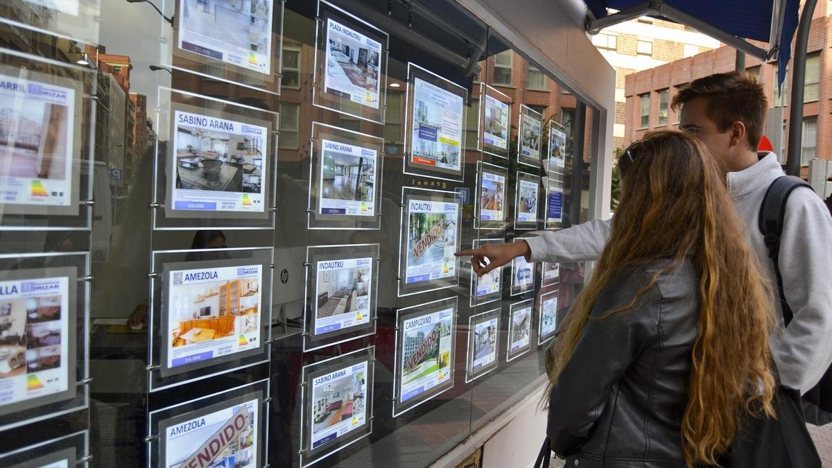 Dos jóvenes buscan piso en el escaparate de una inmobiliaria.