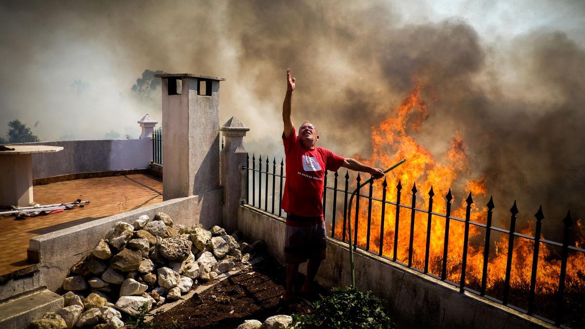 Un vecino pide agua sobre las llamas que avanzan hacia su casa durante el incendio forestal en Canecas, a las afueras de Lisboa.