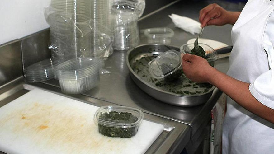 Una empleada de una tienda de comida precocinada, envasando alimentos en la cocina.