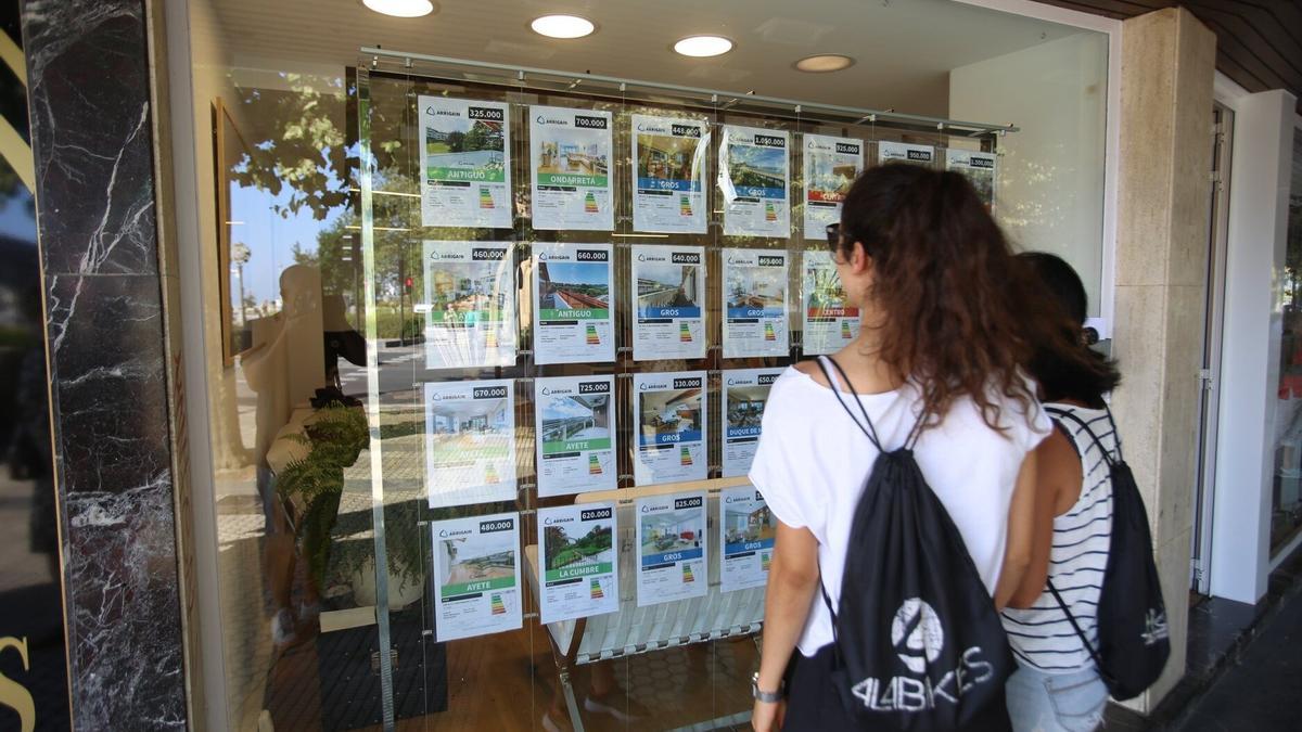 Dos jóvenes consultan precios de viviendas en una inmobiliaria de Donostia.