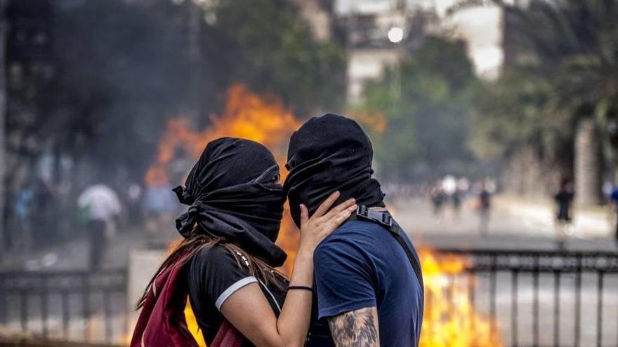 Dos jóvenes encapuchados se besan junto a una barricada en llamas instalada en La Alameda de Santiago.