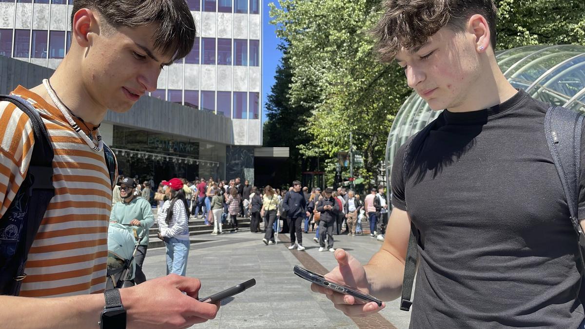 Dos jóvenes consultan sus teléfonos móvil en la plaza Circular de Bilbao