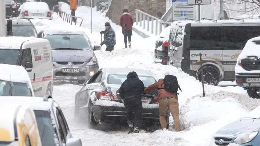 Varias personas empujan un coche atrapado por la nieve caída en una calle del centro de Kiev