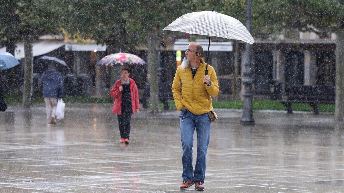 Varias personas se protegen de la lluvia con paraguas en el centro de Pamplona.