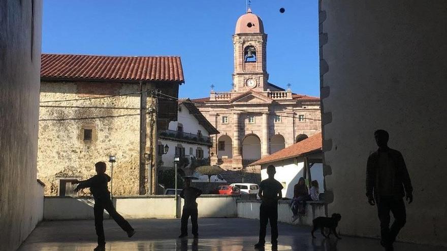 La pelota sobrevuela la iglesia: juez, tanteo y tiempo. Guiño casual de frontones reflejados: bajo el reloj, el elemento de la arquitectura clásica; delante, el del juego de la pelota, entreparedes de la escuela y casa Aldekoa. Juegan: Maite, Ane, Euri, M